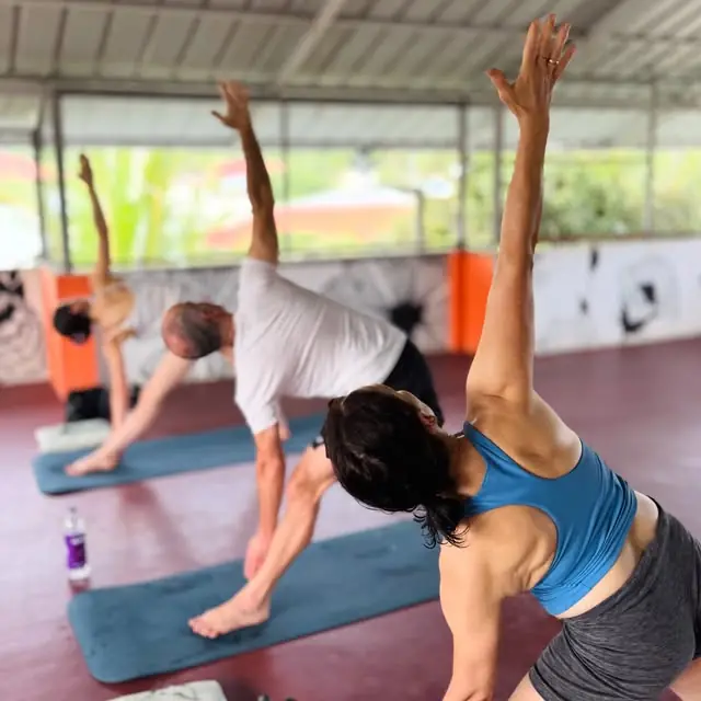 A class reaching into triangle pose under the open rooftop, morning light behind them