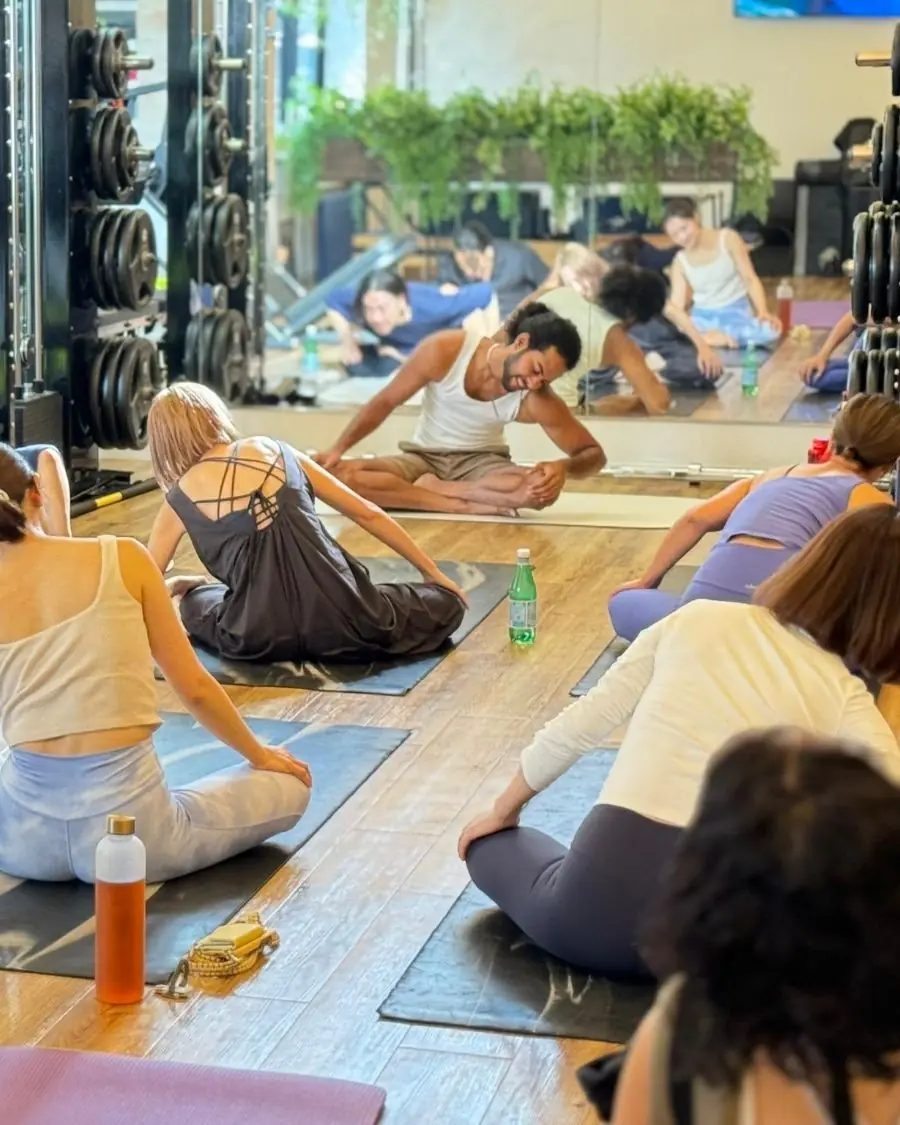 Nithin smiling as he leads a seated stretch for a full class of students on wooden floors in Japan