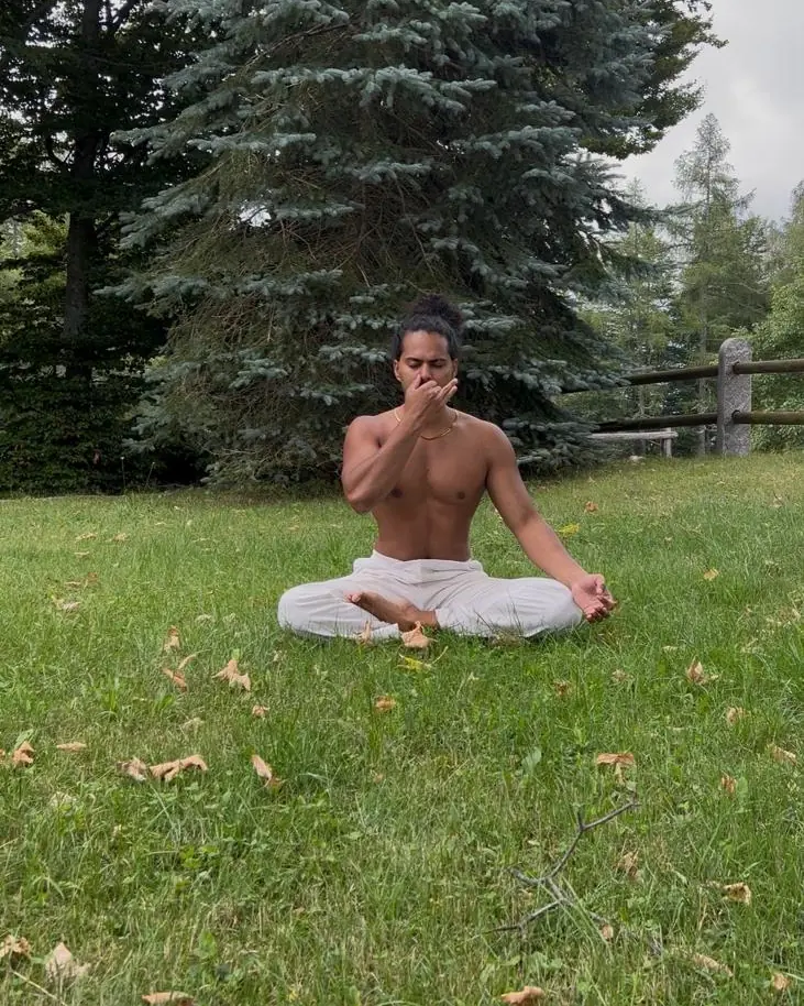 Nithin sits cross-legged on the grass beneath tall pines, practising alternate-nostril breathing