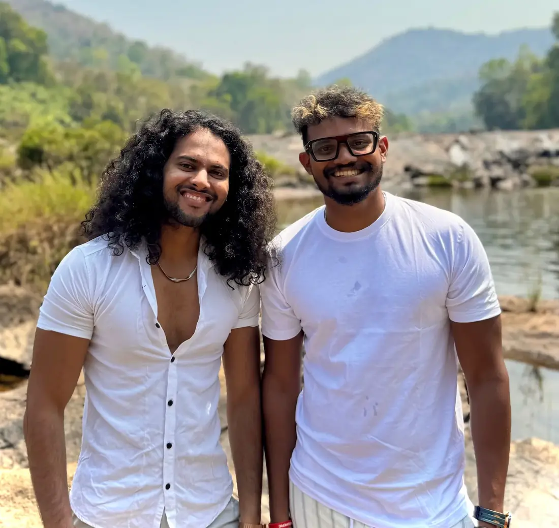 Nithin Xavier and Achu smiling side by side by a river in the Kerala hills