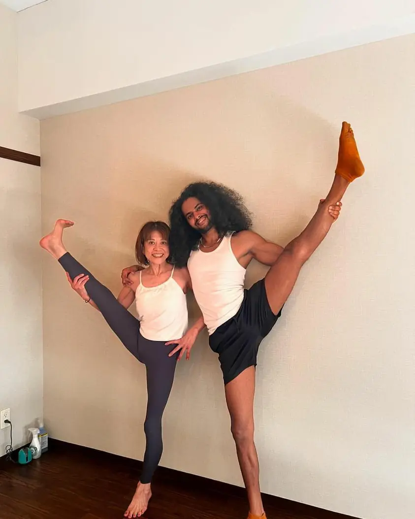 Nithin and a student smile side by side, each holding one leg high in a standing split